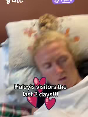 The image features a person lying in bed, appearing to be the creator, with blonde hair and a white t-shirt. Overlayed on the screen are animated pink hearts and text that reads, "Haley’s visitors the last 2 days!!!". The background is a simple brown wall. The overall composition suggests a candid or casual feel.