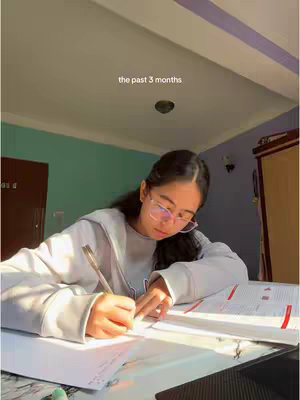A young woman with glasses is seated at a desk with a pen and notebook in hand, writing. The scene is illuminated by sunlight, the room features a teal-colored wall, a light-colored ceiling and a wooden door. Text overlayed says "the past 3 months".