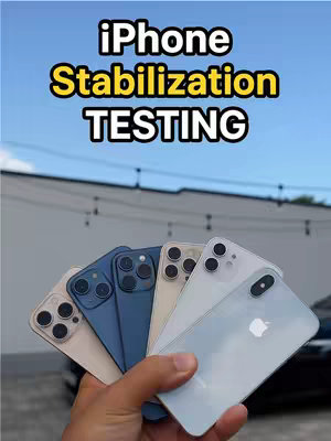 The image presents a hand holding several smartphones. In the background, a blue sky is visible. The smartphones are a mix of black, white, and blue hues. The top text overlay reads 'iPhone Stabilization TESTING'.