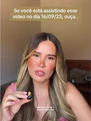 A woman with long blonde hair is centered in the shot, slightly angled and speaking. She's in front of what looks like a neutral-toned background. She's holding a small, circular object in her hand, and wears light makeup with a subtle pink top. The lighting is soft.