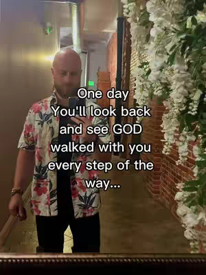A man in a floral shirt and black pants is reflected looking in mirror. Text overlayed on the image in upper right corner reads "One day You'll look back and see GOD walked with you every step of the way..."