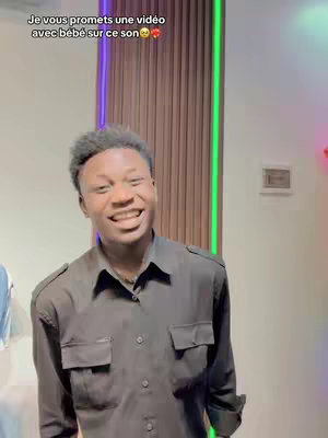 A young man smiles at the camera, with text overlaid at the top. In the background a wooden wall and decorated purple and green neon lights.