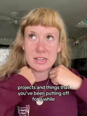 A young woman with blonde chin-length hair and a nose ring looks up and slightly to her left, wearing a maroon long-sleeved shirt. Text appears at the bottom of the frame: 'projects and things that you've been putting off for a while'. The background is a blurred interior with a ceiling fan.