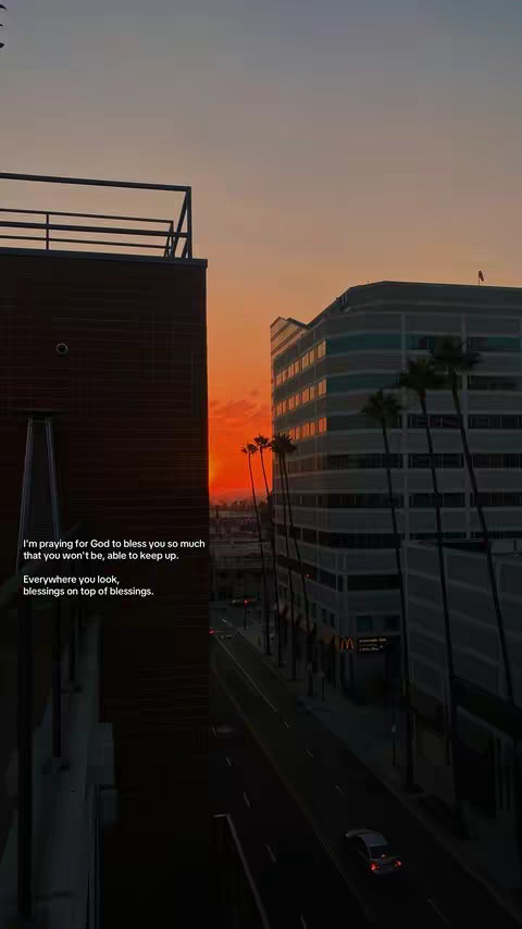 The image is a vertical shot capturing a cityscape at sunset. The sky is filled with warm tones of orange and peach. In the foreground, there are high-rise buildings on the left, with a view of a street and other buildings on the right. Palm trees are visible. The buildings are dark against the colorful sky. Text is overlayed on the image, positioned along the left side. The overall composition creates a serene, contemplative mood.