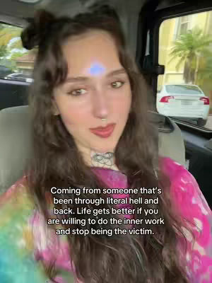A young woman with long, wavy brown hair is seated inside a car. The woman has a nose ring and a tattoo on her neck. She is wearing a tie-dye shirt with shades of pink and green. Text over lays on the image.