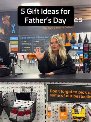 The cover image features a woman standing behind a counter in what appears to be a retail store. Above her head is a black banner with the words "5 Gift Ideas for Father's Day" in white text. The woman is smiling and gesturing with her right hand. Behind her, there’s signage with the text "Bike Services & Protection" with various items displayed on the wall, there is also a sign placed on the counter that reads "Don't forget to pick up some of our bestsellers". The scene is well-lit, with a focus on the woman and the display area below the counter.