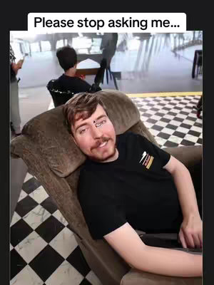A man, presumably MrBeast, is reclined in a brown recliner chair. The background shows a checkered floor and a blurred indoor setting. A text overlay reads, "Please stop asking me...". MrBeast is wearing a black t-shirt and has a drawing on his forehead. The setting appears to be a somewhat informal indoor space.