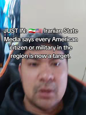 A selfie-style shot featuring a man with short dark hair, positioned from the chest up. He is looking directly at the camera. Overlayed text in white font conveys a news headline related to Iranian state media statements. The background is blurred, suggesting a domestic setting, and the color scheme is neutral, focusing attention on the man and the text.
