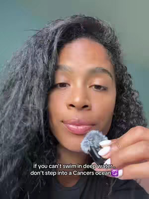 A woman with curly dark hair holds a microphone close to her lips. The background is a plain, light blue-green. Text overlayed on the image reads, "if you can't swim in deep water.. don't step into a Cancers ocean" with a Cancer zodiac symbol.