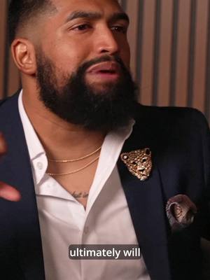 The cover image shows a man wearing a dark suit and a white shirt with a beard. He has a gold necklace and a brooch on his lapel. The background is blurred, and there is text overlaid.