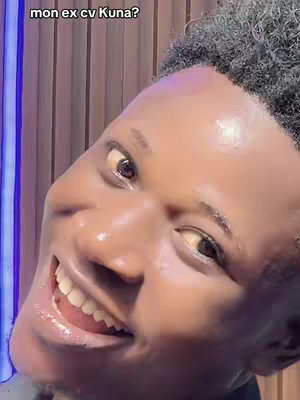 A close-up angled shot features a person's face tilted towards the left. The person's skin appears shiny, possibly due to sweat or a reflective surface. Their eyes are focused, and a broad smile reveals white teeth. The background is a blurred vertical pattern of indeterminate color, adding depth but lacking clear detail. The overall composition is a casual, intimate portrait.
