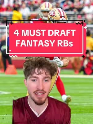 The cover image is a vertical video shot. It features a man with curly hair in the bottom center, looking at the viewer and speaking. He's positioned on a grassy field with a blurred background featuring a football stadium with players in the distance. Superimposed over the image is a red rectangular box, containing the text '4 MUST DRAFT FANTASY RBs' in white.