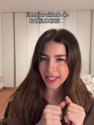 A woman with long brown hair is in a room speaking. Above her head is a superimposed text that says "El mejor airbnb de BARILOCHE".