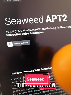 Close-up of a computer screen displaying text, partially obscured by a blurred orange shape in the foreground. The screen shows the title 'Seaweed APT2' in large, white font, followed by smaller text describing 'Autoregressive Adversarial Post-Training for Real-Time Interactive Video Generation' then the text is covered by a pink box. The overall composition is a mix of sharp and soft focus, with a dark, tech-related setting.