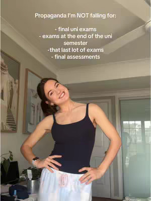 A young woman with dark hair, pulled back in a ponytail, smiles and leans slightly to the left. She wears a black tank top and white and light blue pajama pants, standing in what appears to be a room with light-colored walls and a framed picture behind her. Text is layered over the image.