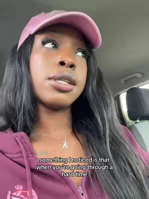 A woman in a pink baseball cap and a maroon hoodie looks off-camera expressing a thoughtful emotion, sitting inside a car. Text is overlaid at the bottom of the image.