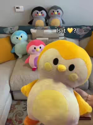 The cover image shows several plush penguin toys of various colors sitting on a gray couch with a patterned cushion behind them. In the foreground a big yellow penguin toy. Overlaid on the image is text questioning 'Is it ❤️?'