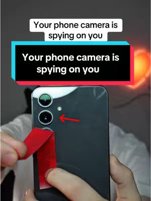 The image shows a close-up view of a phone with a red sticker being peeled off the camera lenses. Text overlays state 'Your phone camera is spying on you'. Additional text appears on a layered background.