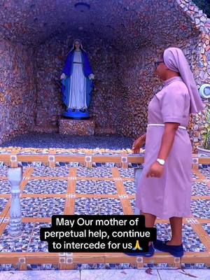 The image shows a woman dressed in a lilac dress and head wrap standing to the right of a shrine honoring The Mother of Perpetual Help, a statue of Mary. Below, a text box reads, \"May Our mother of perpetual help, continue to intercede for us.\"