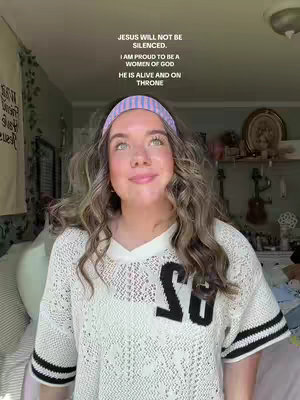 A young woman with long wavy blonde hair and a pink headband stands in front of a window and a wall adorned with items. She is wearing a white sweater with black detailing and the letters "SU" on the front and appears to be looking upwards with a slight smile. Overlayed text in a sans-serif font is composed at the upper-center of the frame.