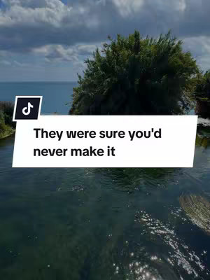 A serene view of a body of water with a shoreline in the background. Above the water rises a screen with text overlayed upon it, in the background there's what looks like a tree line or cliff.