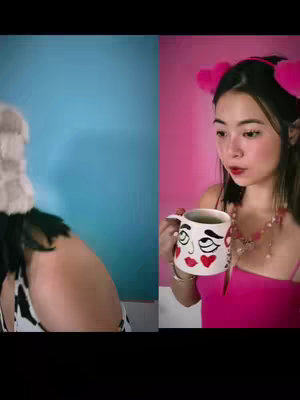 The cover image is split vertically with two sides. On the left, a person is seen from the shoulders up; their face is obscured by what appears to be a furry, head-covering accessory with a cow-print top. The background is a solid blue. On the right, a young woman is positioned holding a mug with a cartoon-like face design on it. She wears a pink top and pink, heart-shaped hair accessories, against a pink backdrop.
