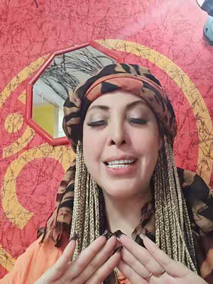 The cover image features a woman with a headscarf and braids looking at the camera. She has her hands in front of her. Behind her is a red wall with a gold design, and a mirror in the background.