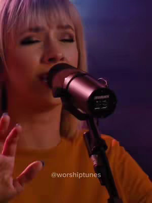 The cover image features a woman singing into a microphone. She is wearing a yellow top, and her blonde hair is styled with a side part. The background is blurred and deep purple. The shot is framed from the shoulders up, focusing on her face and the microphone.