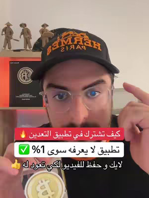 A man wearing glasses and a black Hermes cap is pointing up with his right index finger. The background features art pieces, books, and a shelf that is lit up with orange light.