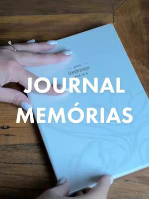 The cover image displays a journal held open, with a woman's hand on the edge. White text reading 'JOURNAL MEMÓRIAS' are in white overlaid on the journal with a subtle marble design.
