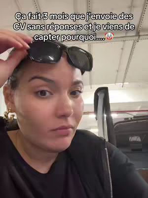 A selfie-style shot featuring a woman looking directly at the camera with a slightly concerned expression. She is wearing sunglasses perched on her head. The background appears to be an interior space with overhead lighting and some equipment visible.