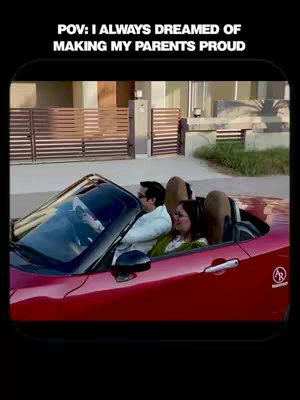 A man is driving a red convertible, with his mother sitting next to him. The image is framed with a black border, and the background shows a house and a bright sky. Text overlaying the image reads, 'POV: I ALWAYS DREAMED OF MAKING MY PARENTS PROUD'.