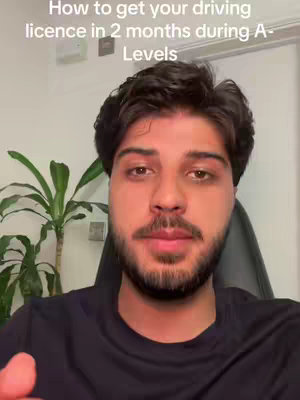 A selfie-style video featuring a young man as the primary subject. The man is positioned in the center of the frame, looking directly at the camera. The background includes a nondescript interior setting with a green plant and a wall. The lighting appears to be natural, and the overall composition is simple and direct, focusing on the man's upper body and face.
