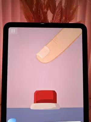 A close-up of a tablet screen displaying a game interface. A cartoonish finger with a manicured nail is hovering above a red button. The background is a soft pink with a blurred, decorative element at the top of the screen.