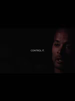 A dark, dramatic image featuring a dark-skinned man's face in the right half, a stark black background, and minimal text. The man is looking towards the left of the frame, his expression a mixture of seriousness, The text 'CONTROL IT.' is positioned centrally on the left side.