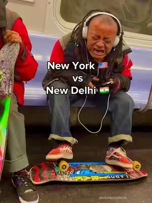 The image shows a person sitting on a skateboard inside what appears to be a subway car. The person has dreadlocks, is wearing headphones, and has a very expressive, distressed face. They are sitting with their legs spread, with a skateboard placed between them. The text overlay reads 'New York vs New Delhi' with flags of the USA and India. The layout is vertical, with the main focus on the person's emotional expression.