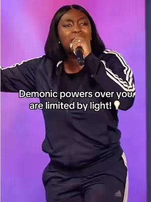 A woman with dark hair and a black Adidas tracksuit is holding a microphone and appears to be passionately speaking or singing. Text overlayed on the image states: Demonic powers over you are limited by light!