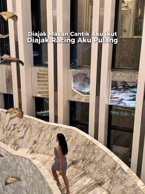 A woman is ascending a staircase with a marble facade. The interior is contemporary, with large windows and ornate decorations.