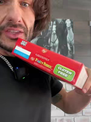 A medium shot features a man holding a red cereal box with the words "Fruity Pebbles" and "Gluten Free" visible. He is positioned with the box partially obscuring his face, and the backdrop includes a shadowy image of people on horseback.