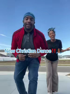 An outdoor shot featuring two people dancing, a man and a woman, both smiling at the camera. The man is in the foreground, wearing a red jacket over a grey shirt and blue jeans, and a blue doo-rag. The woman is slightly behind to the right in a black shirt and tan pants. Text overlays the image, reading 'New Christian Dance !!'. The background is a clear, light blue sky.