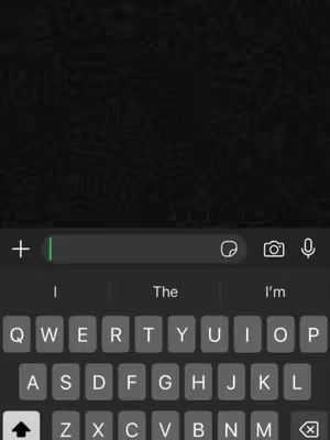 The image shows a close-up of a smartphone screen displaying a messaging app interface. A keyboard is visible at the bottom, with suggested words above it. The background is a dark, textured pattern. The top shows a text input bar with a plus button and a search icon.