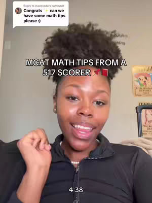 A woman with dark skin and curly dark hair is the primary focus of the image. She has a light complexion and is smiling slightly while looking off to the side. She is wearing a black top and a white pearl necklace. The text overlay reads "MCAT MATH TIPS FROM A 517 SCORER." In the background, there is a glimpse of a wall and what appears to be a framed picture or poster.