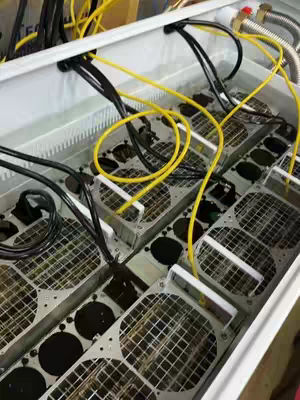 The cover image shows a close-up of the inside of a container filled with liquid, resembling water or a cooling fluid. Submerged within the liquid are several rows of metal components, possibly servers or mining equipment, with gridded surfaces and intricate wiring. Yellow and black cables snake around the components, and the overall composition highlights a technological setup designed for processing or cooling operations. The lighting reflects off the liquid and metal, enhancing the details of the machinery and the electrical components.