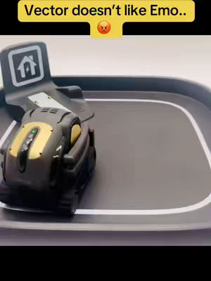 The image displays a black and gold robot-like device on a gray circular track with a white border. A text overlay in a yellow box reads, 'Vector doesn't like Emo..' and an angry face emoji sits on the right.