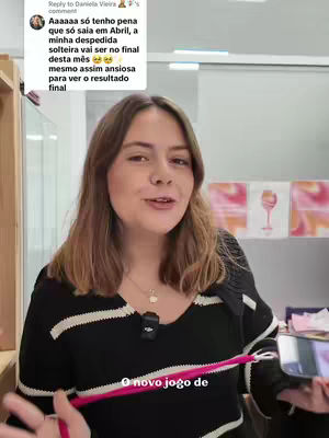 A woman with long brown hair smiles at the camera, wearing a black and white striped sweater. She is holding a pink cord in her hands. The background is blurred but appears to be an interior setting.