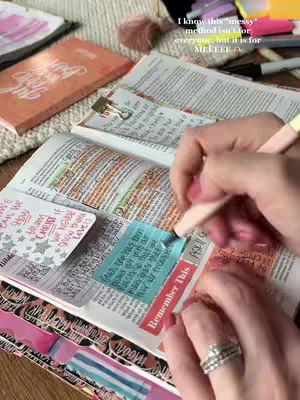 A person is shown highlighting and taking notes in an open Bible. The Bible is in a cozy setting, with a soft blanket visible in the background. The person's hands are the main focus, adorned with a ring, holding a pen and interacting with the pages. The overall image has a warm, inviting feel.