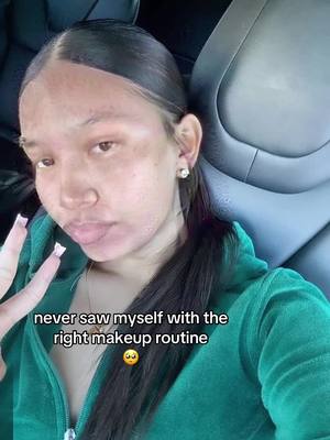 A selfie shows a young woman in a green zip-up hoodie inside a car. She's making the peace sign with her left hand near her face, with the index and middle fingers extended. Her expression is neutral, with her lips slightly pursed. Text overlayed at the bottom reads: 'never saw myself with the right makeup routine' with a sad face emoji