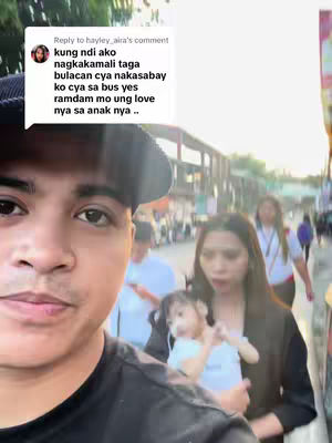 The cover image is a selfie taken by a man, featuring a woman holding a baby, and other people in the background. The man is in the foreground, and a text overlay is present in a white speech bubble that starts from another user reply. The shot appears to be taken outdoors on a sunny day.