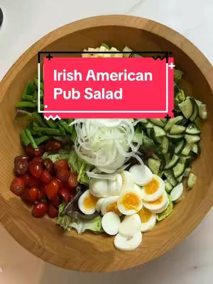 A wooden bowl filled with a colorful salad. The salad includes Boston butter lettuce, cucumbers, tomatoes, boiled eggs, extra sharp cheddar cheese, blanched green beans, and pickled beets. A red rectangle with white text overlays the center of the bowl.