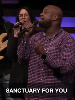The cover image shows two people, a woman and a man, singing into microphones during what appears to be a worship service. The man is in the foreground, wearing a plaid shirt, and the woman is behind him to the left with glasses. The text overlayed at the bottom reads 'SANCTUARY FOR YOU'. The lighting is dim with a dark background.